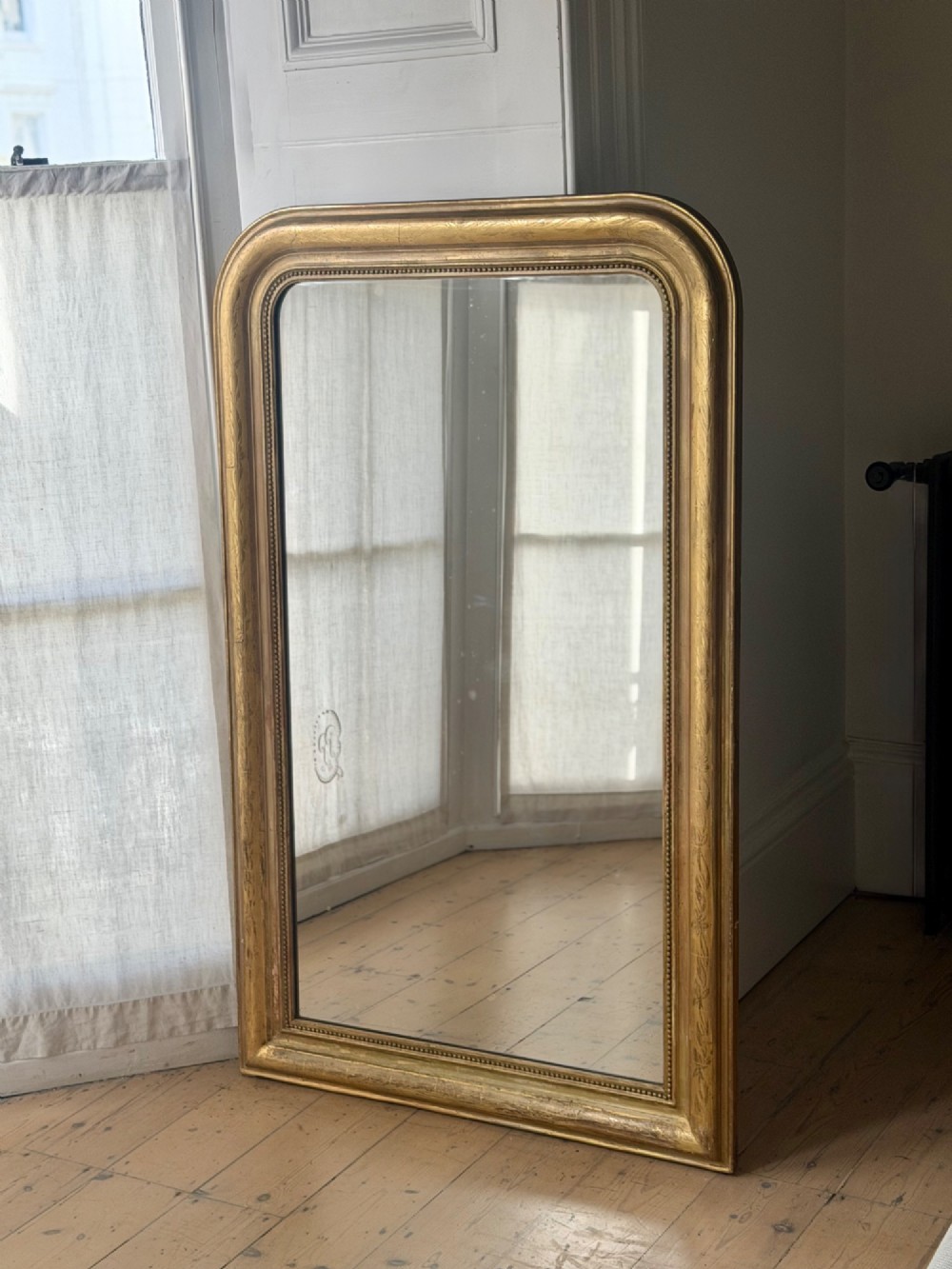 A mid-19th-century French Louis Philippe mirror featuring a gilded frame with rounded upper corners and subtle beaded detailing.