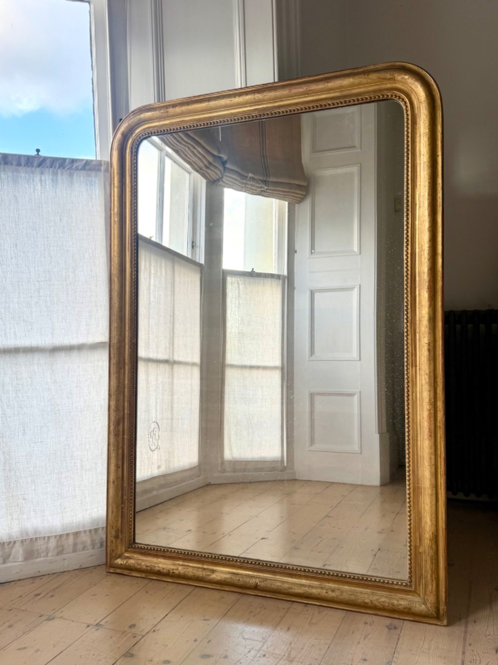 Large rectangular French Louis Philippe mirror featuring rounded upper corners, a beaded inner border, and a gilded finish.