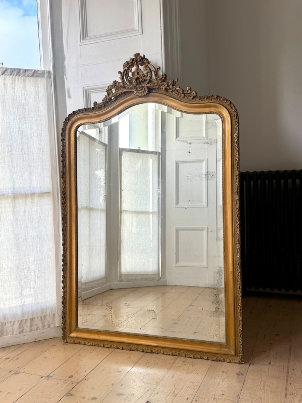 A large French Louis XV style giltwood mirror featuring an arched top crest with carved scrollwork and a bevelled mirror plate.