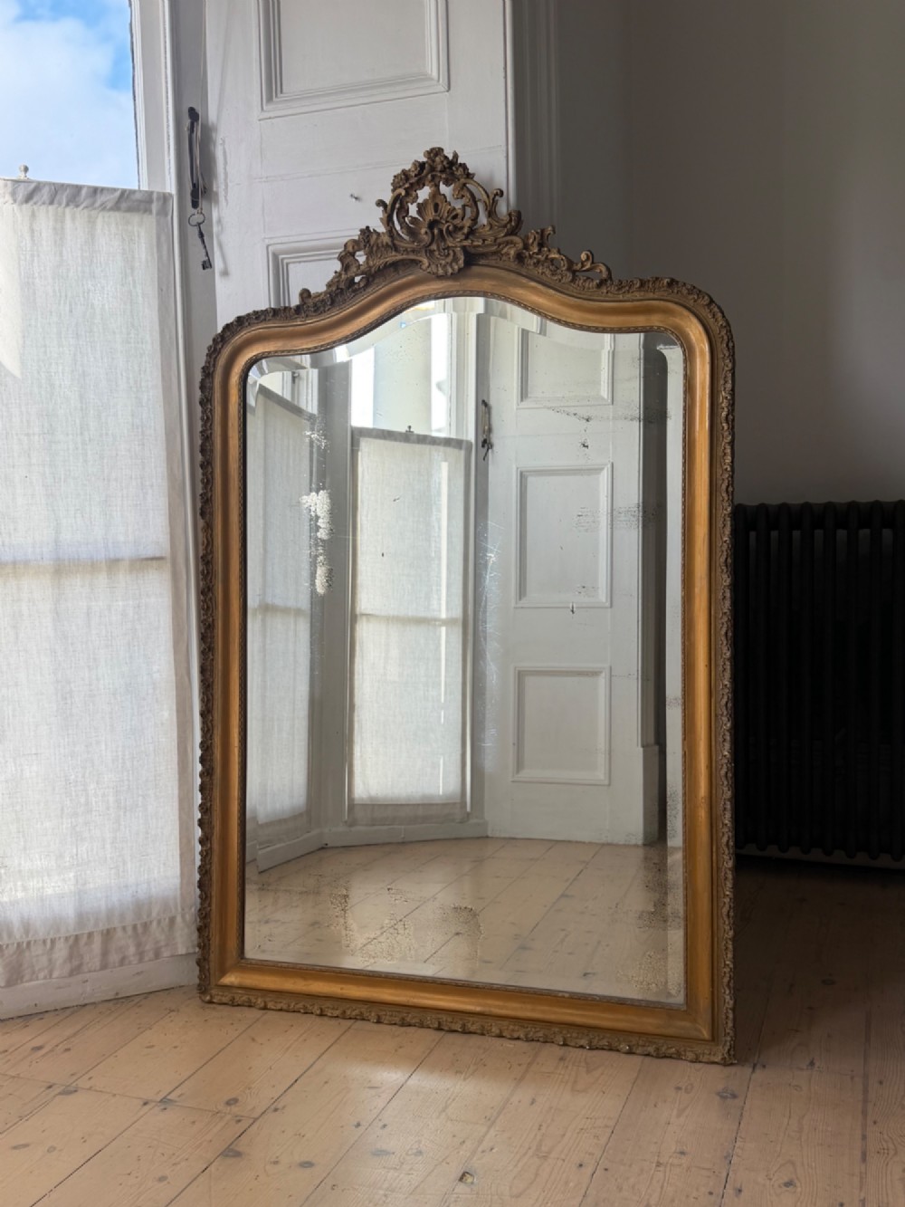 A large French Louis XV style giltwood mirror featuring an arched top crest with carved scrollwork and a bevelled mirror plate. View II