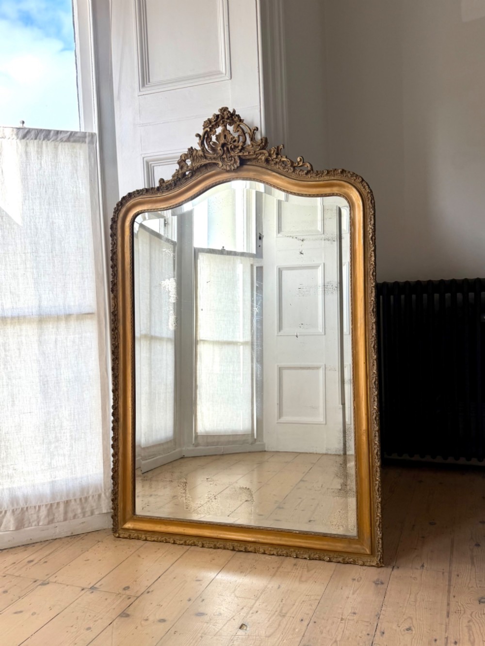 A large French Louis XV style giltwood mirror featuring an arched top crest with carved scrollwork and a bevelled mirror plate. View IV