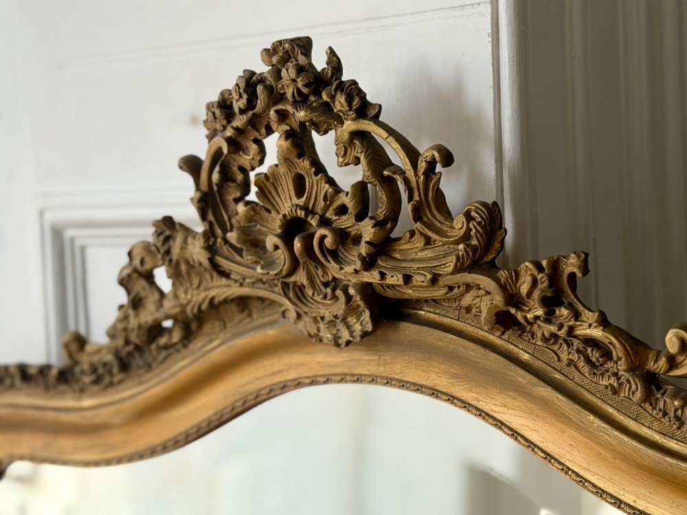 A large French Louis XV style giltwood mirror featuring an arched top crest with carved scrollwork and a bevelled mirror plate. View V