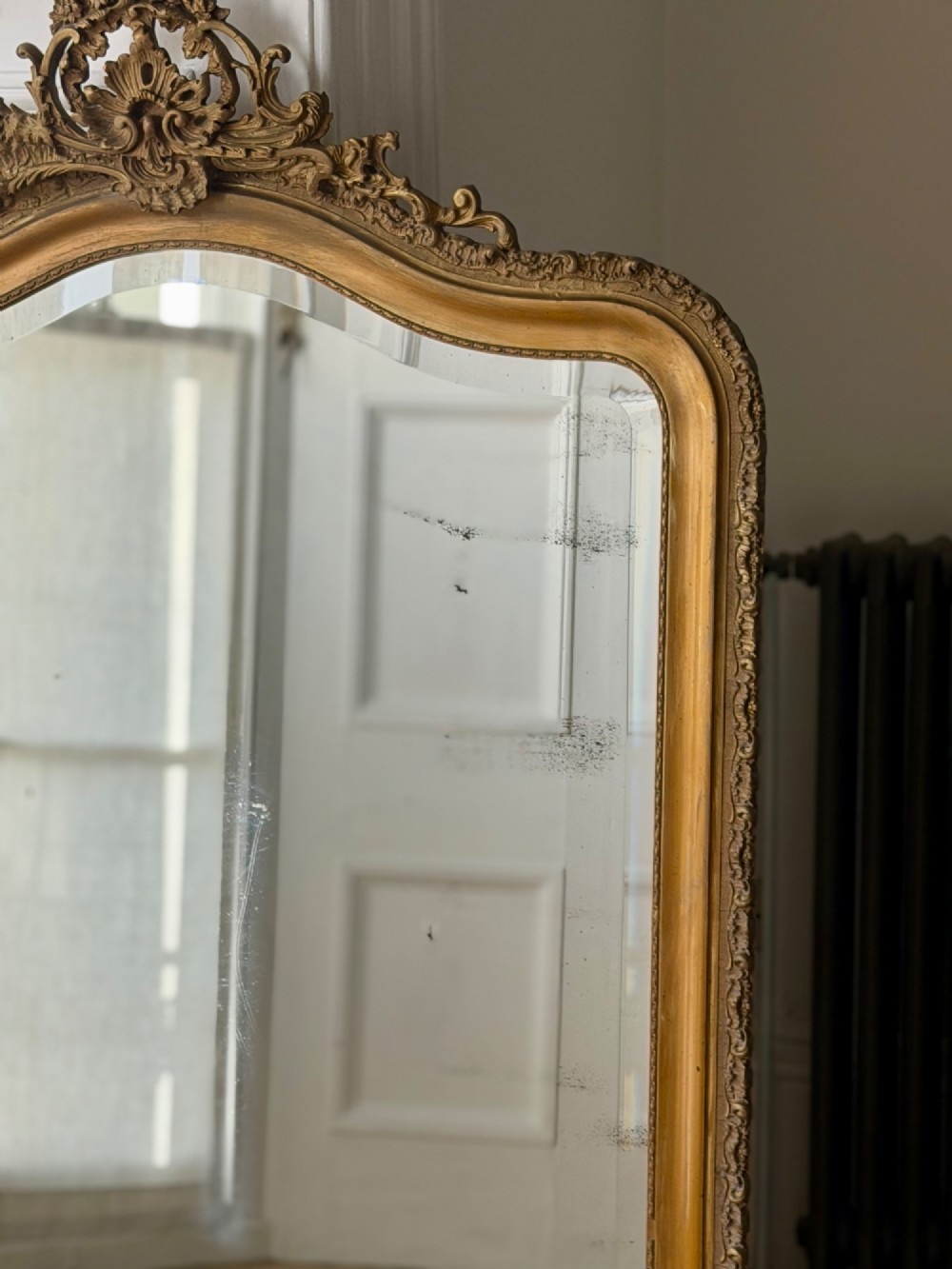A large French Louis XV style giltwood mirror featuring an arched top crest with carved scrollwork and a bevelled mirror plate. View IX