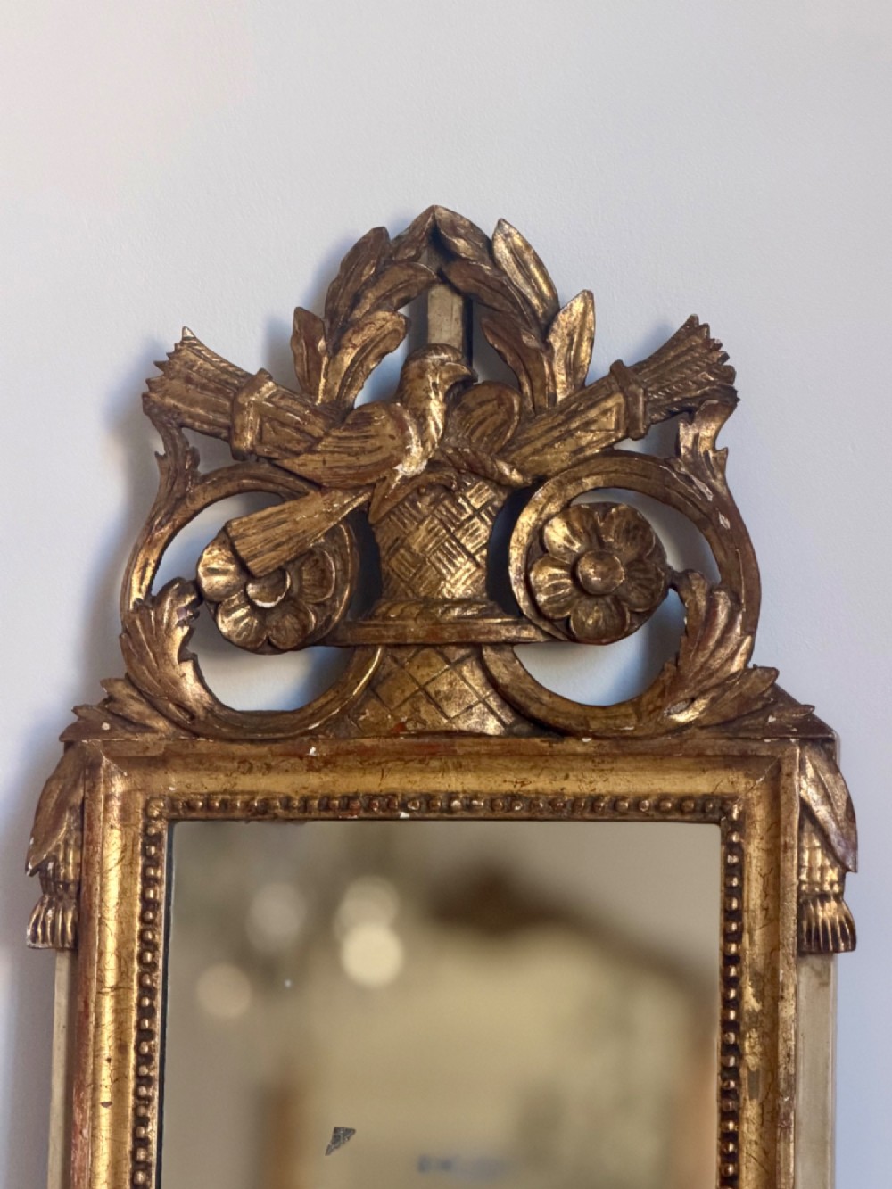 An 18th-century French giltwood wall mirror featuring a carved bird crest, beaded border, and foxed reflective glass. View II