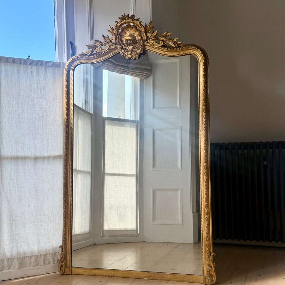 A large antique French giltwood mirror featuring an arched top decorated with a central shell crest and floral leaf details. View III