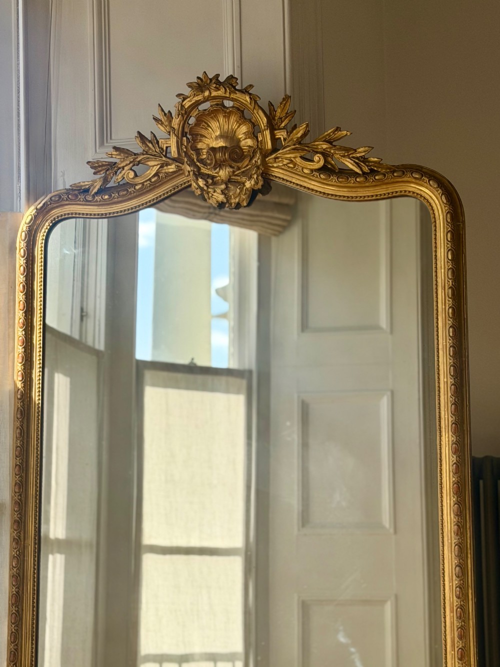 A large antique French giltwood mirror featuring an arched top decorated with a central shell crest and floral leaf details. View IV