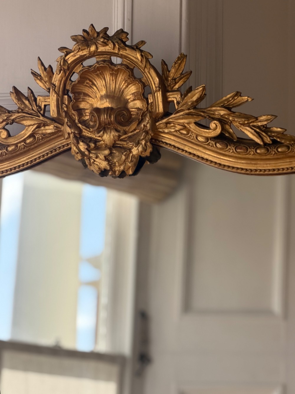 A large antique French giltwood mirror featuring an arched top decorated with a central shell crest and floral leaf details. View V