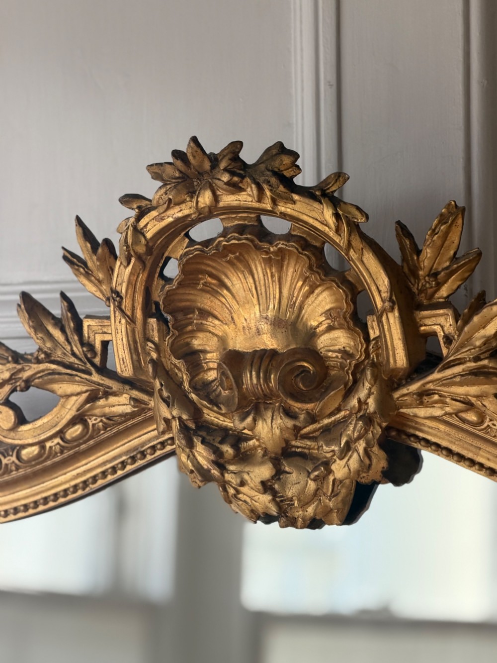 A large antique French giltwood mirror featuring an arched top decorated with a central shell crest and floral leaf details. View VI
