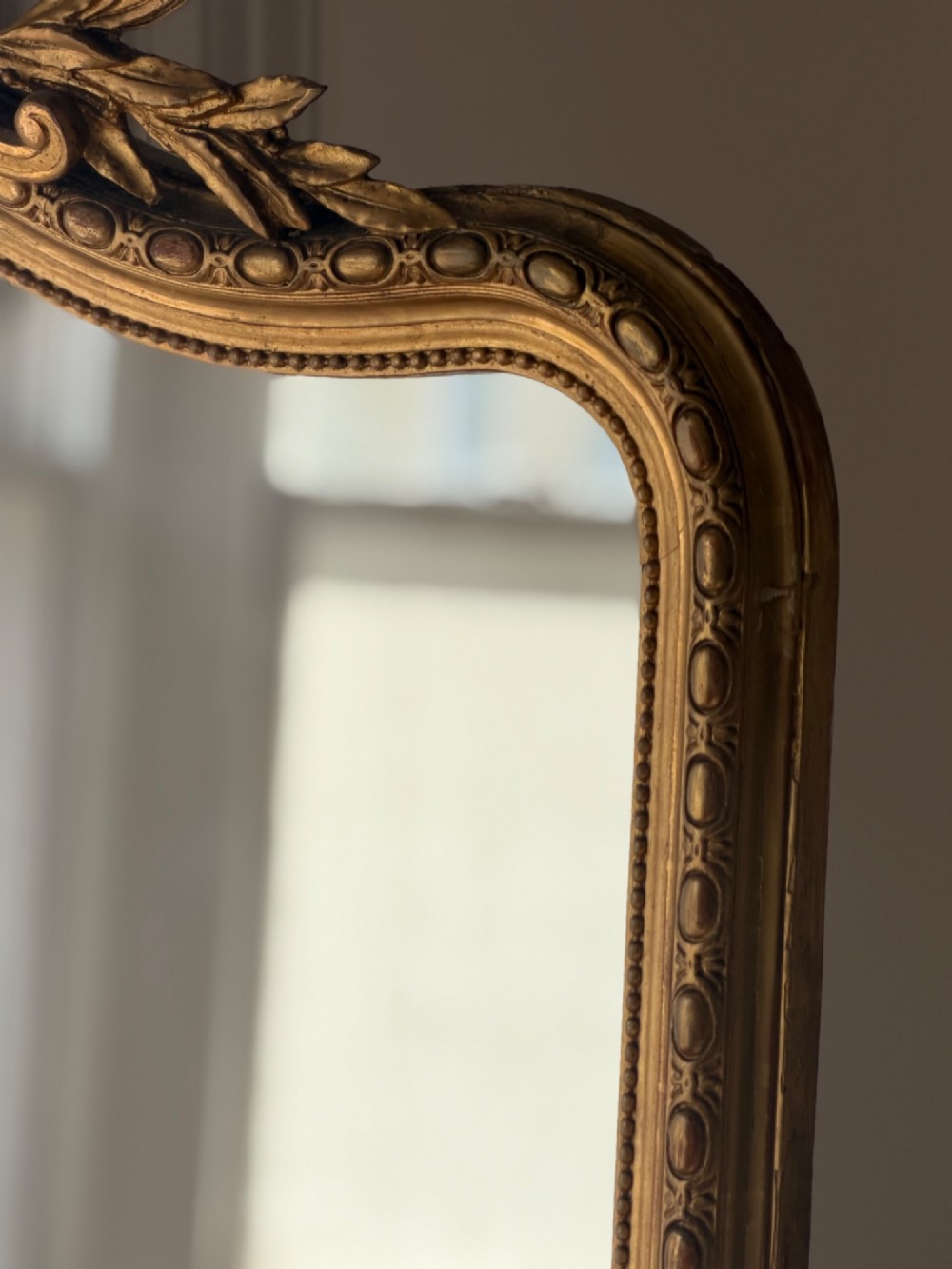 A large antique French giltwood mirror featuring an arched top decorated with a central shell crest and floral leaf details. View XI