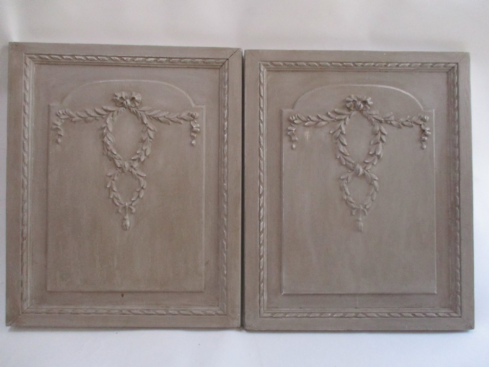 A pair of grey painted wooden cabinet doors decorated with hand-carved laurel wreaths and ribbon swags.