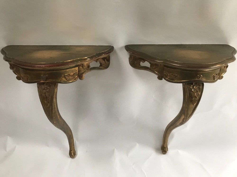 A pair of wall-mounted Italian giltwood console tables with serpentine tops, carved floral aprons, and single cabriole legs.