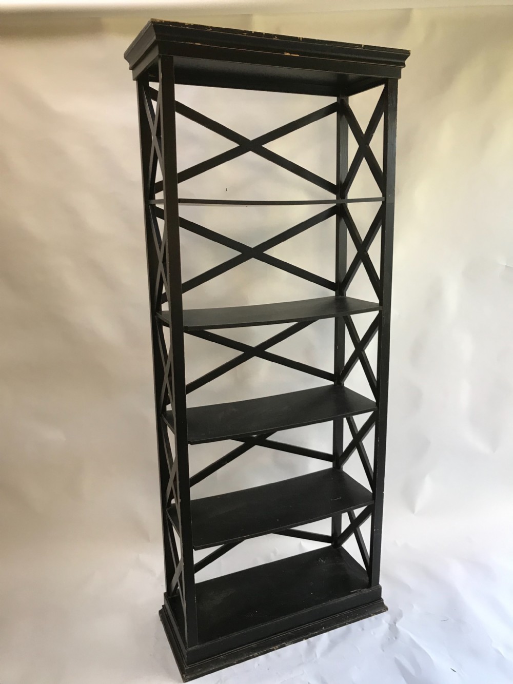 A tall, freestanding black painted open shelving unit featuring five horizontal tiers, X-frame lattice sides, a moulded top cornice, and a plinth base.