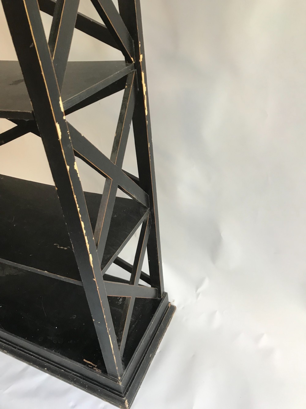 A tall, freestanding black painted open shelving unit featuring five horizontal tiers, X-frame lattice sides, a moulded top cornice, and a plinth base. View III
