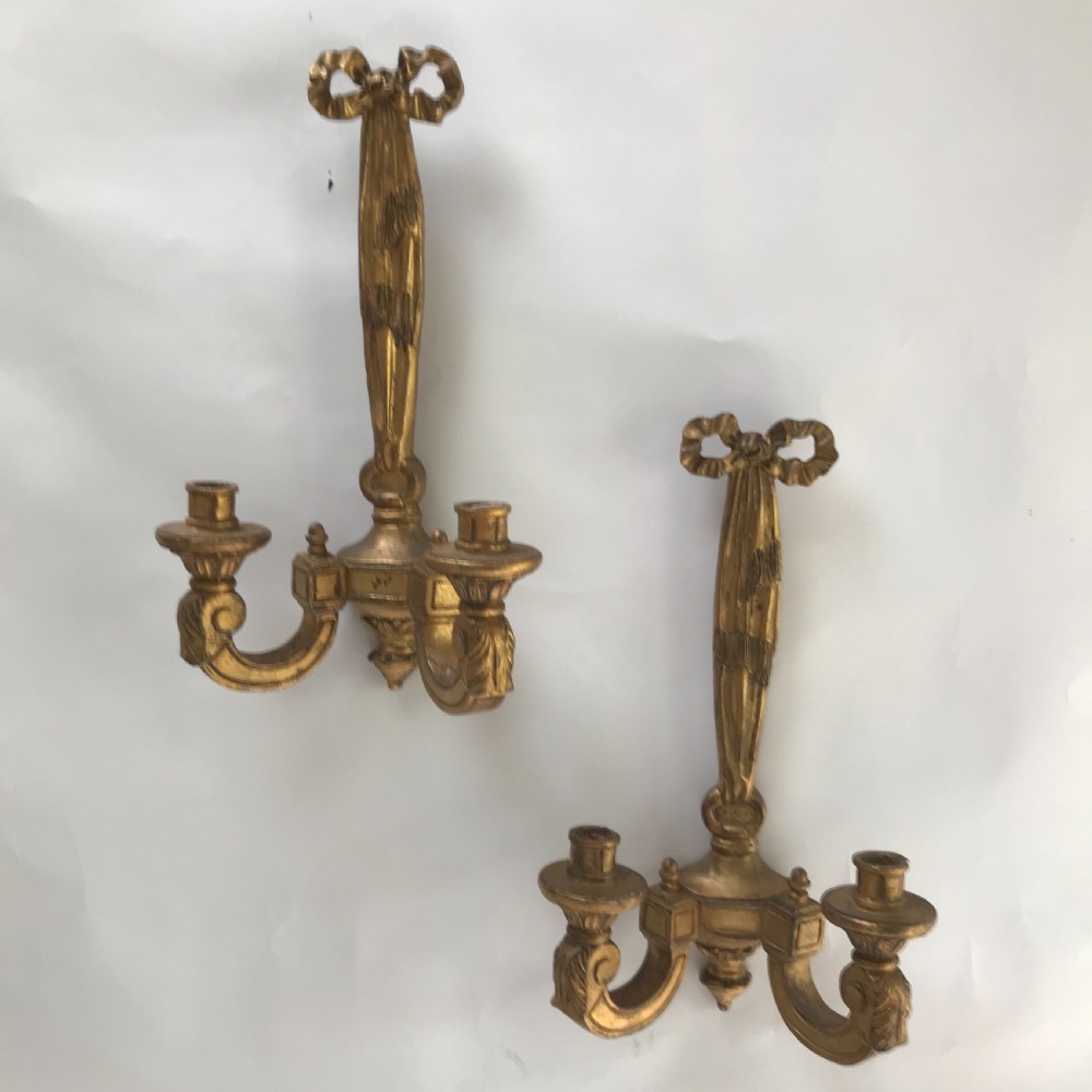 A pair of French carved giltwood wall lights featuring ribbon bow backplates and two scrolling candle arms with acanthus leaf decoration.