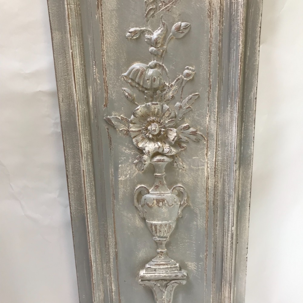 A vertical painted grey wood panel featuring an arched frame encircling a hand-carved classical urn and floral relief. View II