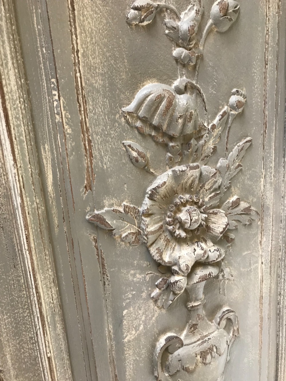 A vertical painted grey wood panel featuring an arched frame encircling a hand-carved classical urn and floral relief. View VIII