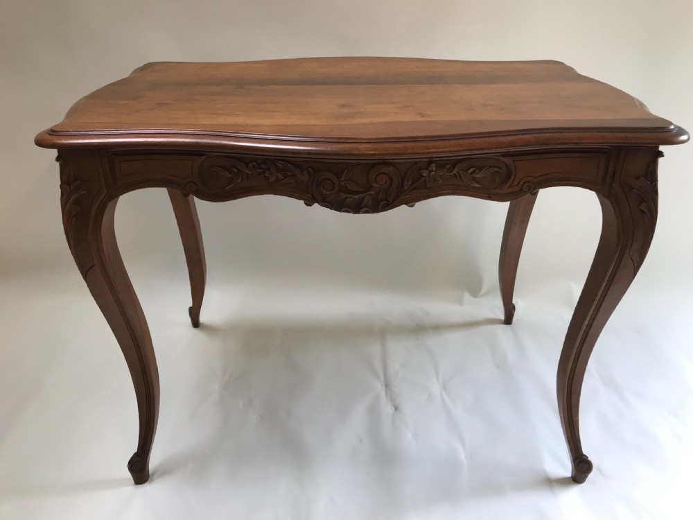 An antique French walnut centre table featuring carved floral frieze detailing and slender cabriole legs with a serpentine top.