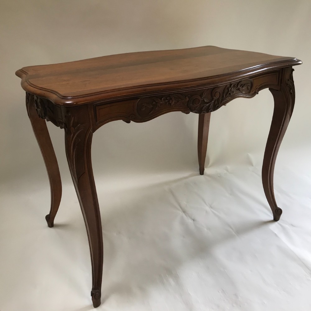 An antique French walnut centre table featuring carved floral frieze detailing and slender cabriole legs with a serpentine top. View V
