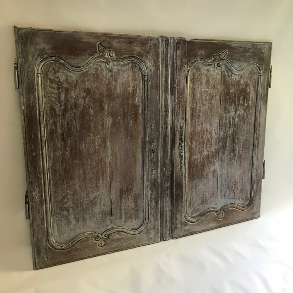 A pair of antique French carved wooden doors featuring a distressed grey painted finish, moulded serpentine panels, and original iron hinges.