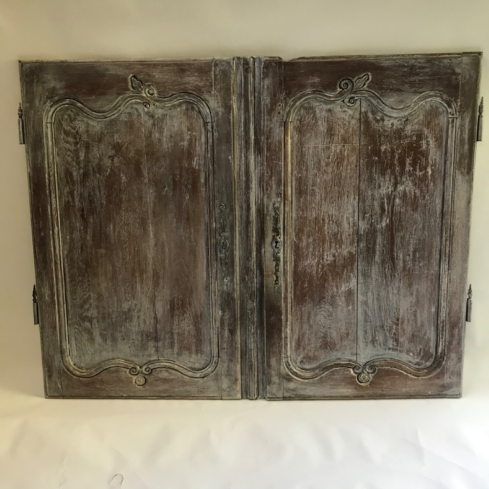 A pair of antique French carved wooden doors featuring a distressed grey painted finish, moulded serpentine panels, and original iron hinges. View II