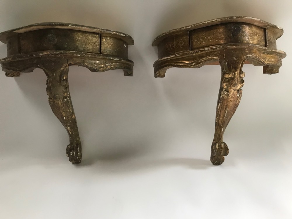 A pair of small wall-mounted Italian giltwood console tables with single carved cabriole legs and detailed aprons.