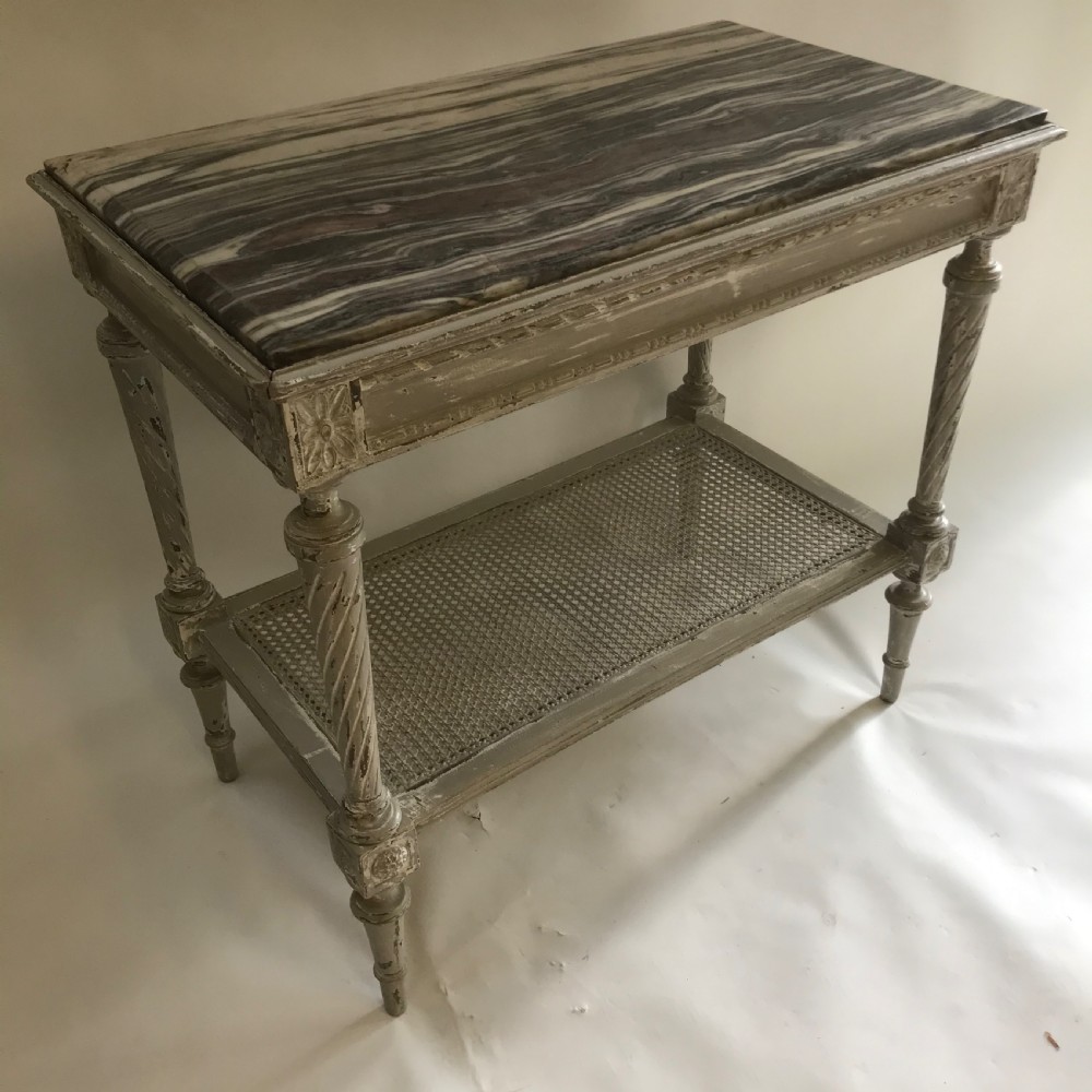 A French Neoclassical style painted wooden side table featuring a dark striated marble top, spiral turned legs, and a woven cane lower shelf.