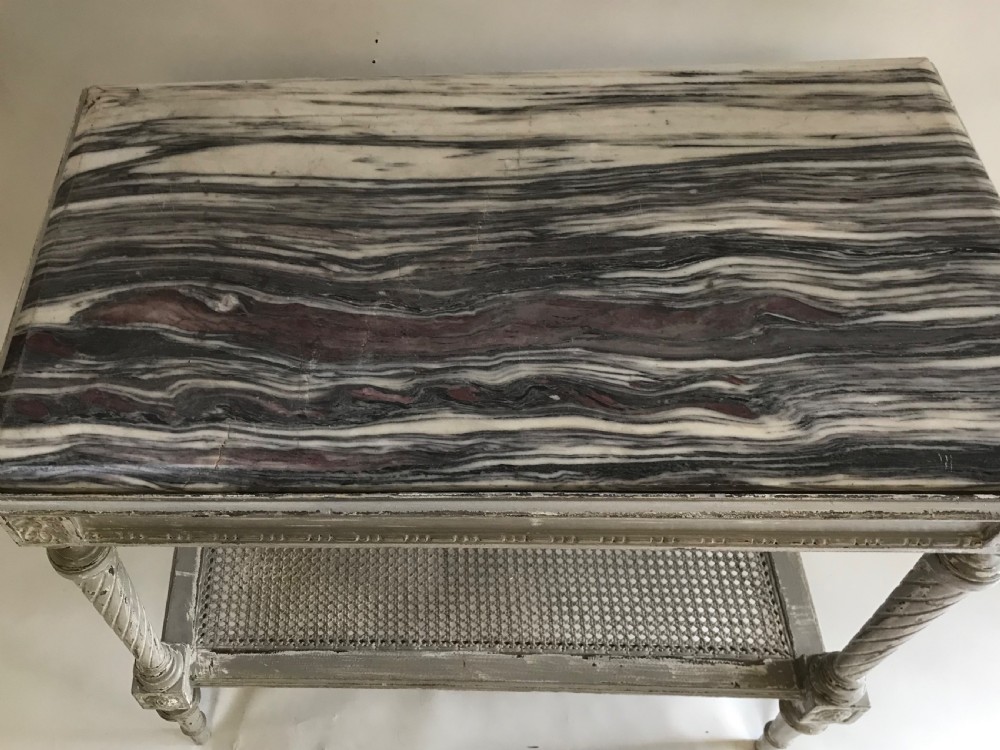 A French Neoclassical style painted wooden side table featuring a dark striated marble top, spiral turned legs, and a woven cane lower shelf. View IV