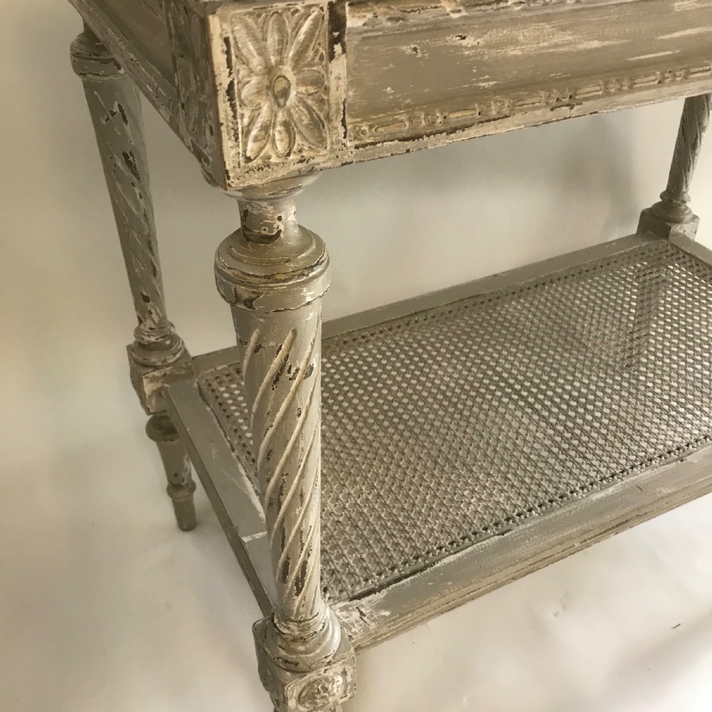 A French Neoclassical style painted wooden side table featuring a dark striated marble top, spiral turned legs, and a woven cane lower shelf. View VI