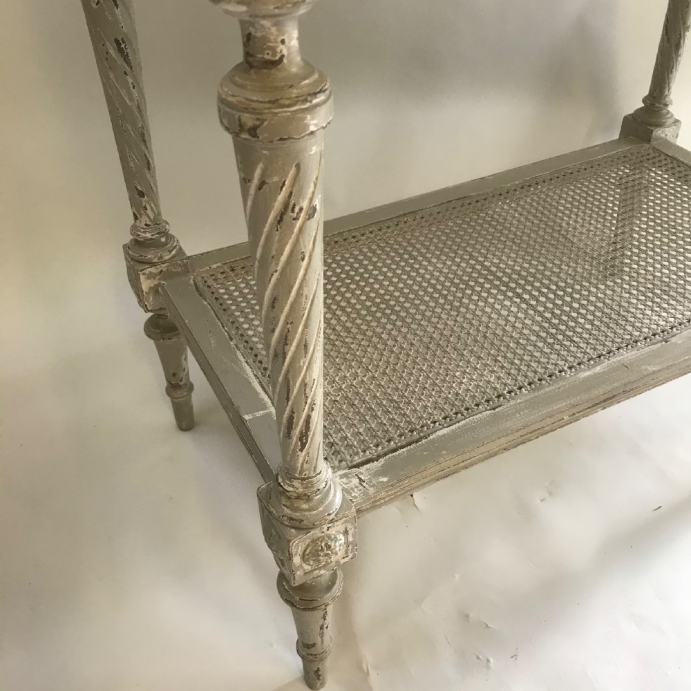 A French Neoclassical style painted wooden side table featuring a dark striated marble top, spiral turned legs, and a woven cane lower shelf. View VII