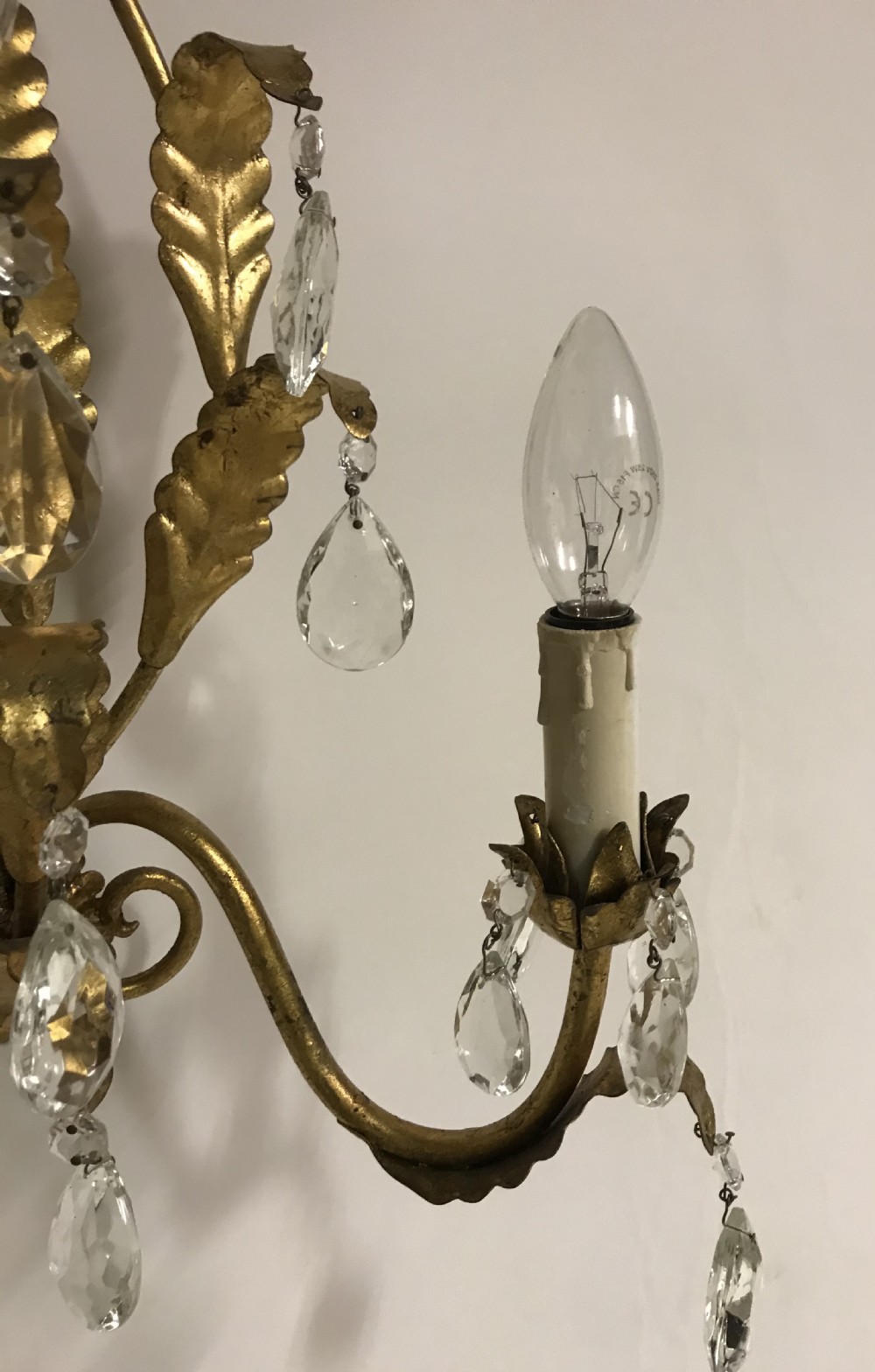 A pair of gilded metal two-arm wall sconces decorated with leaf forms, tulip-shaped flower candle sockets, and suspended clear crystal drops. View III