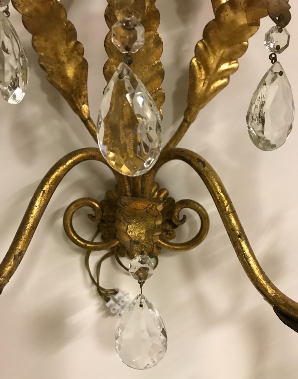 A pair of gilded metal two-arm wall sconces decorated with leaf forms, tulip-shaped flower candle sockets, and suspended clear crystal drops. View V