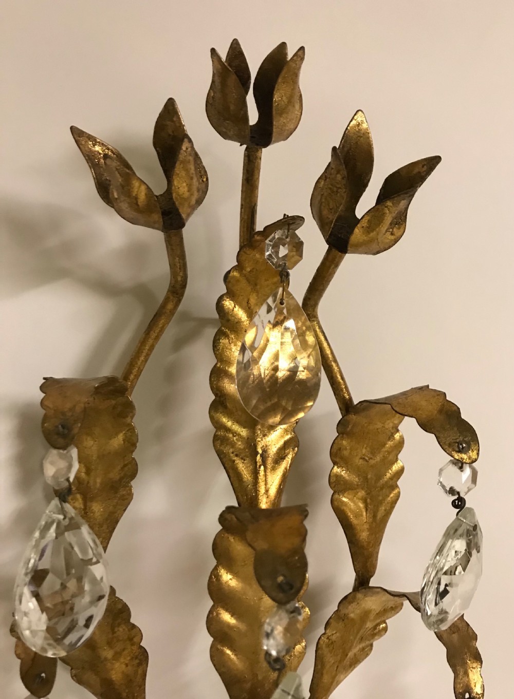 A pair of gilded metal two-arm wall sconces decorated with leaf forms, tulip-shaped flower candle sockets, and suspended clear crystal drops. View VI