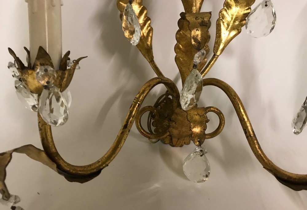 A pair of gilded metal two-arm wall sconces decorated with leaf forms, tulip-shaped flower candle sockets, and suspended clear crystal drops. View VII