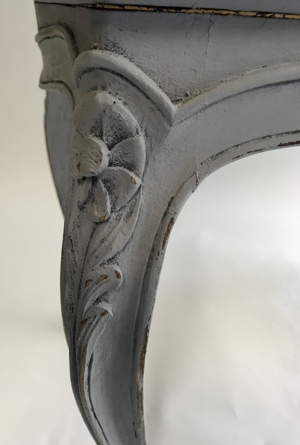 A rectangular grey painted French stool featuring a hand-woven cane top, floral carved apron, and cabriole legs. View III