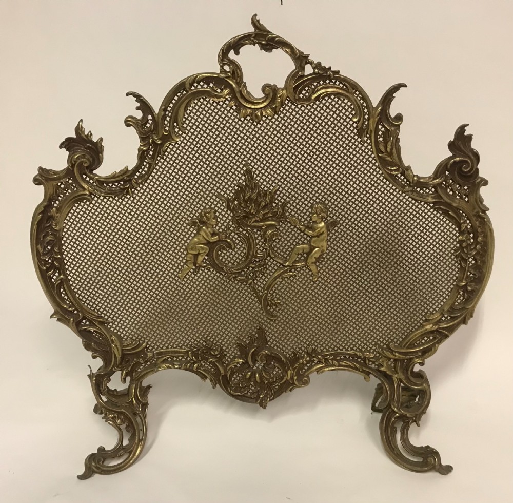 An ornate French Rococo style gilded bronze fire screen with a central cherub motif and fine metal mesh.