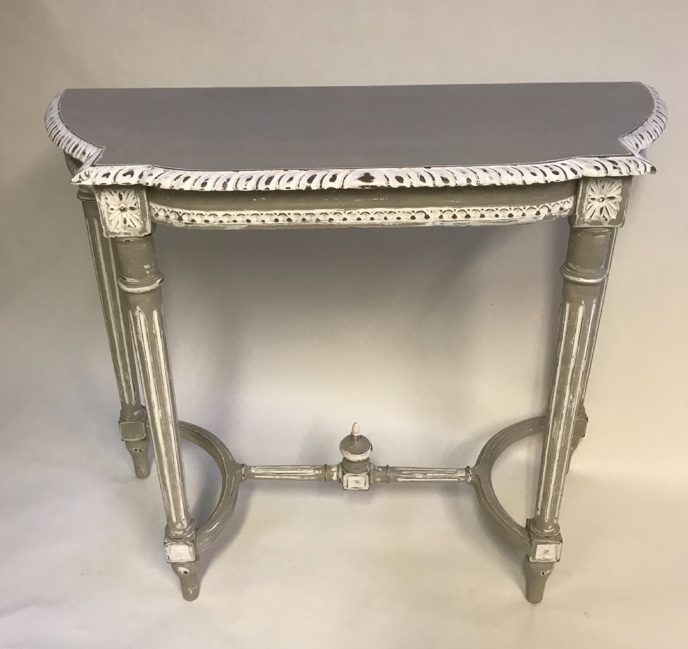 A French Louis XVI style painted console table in grey and white featuring fluted legs, carved rosettes, and an arched stretcher with a central finial.