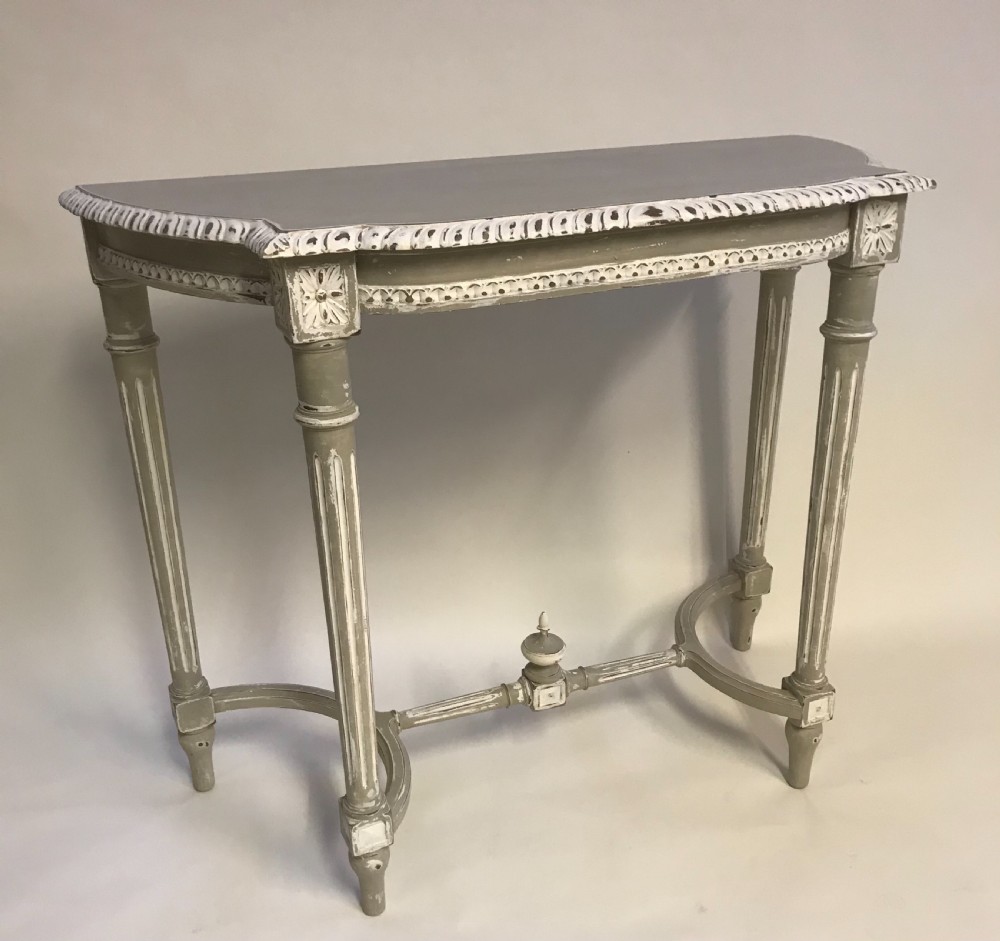 A French Louis XVI style painted console table in grey and white featuring fluted legs, carved rosettes, and an arched stretcher with a central finial. View IV