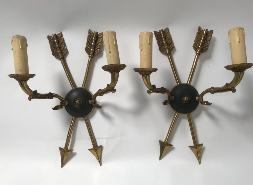 A pair of French brass twin-arm wall lights with a crossed arrow motif and dark circular backplates.