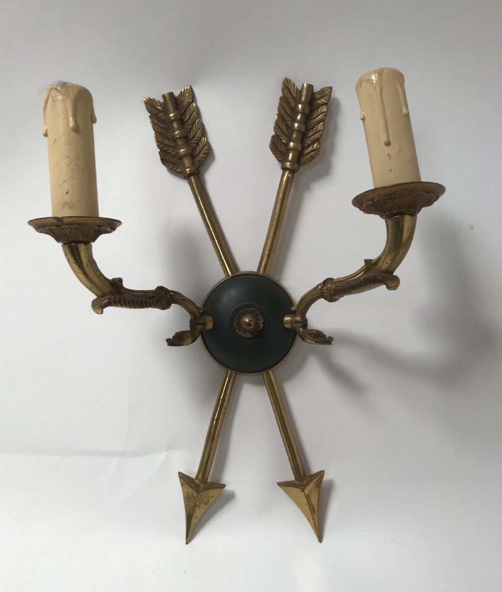 A pair of French brass twin-arm wall lights with a crossed arrow motif and dark circular backplates. View II