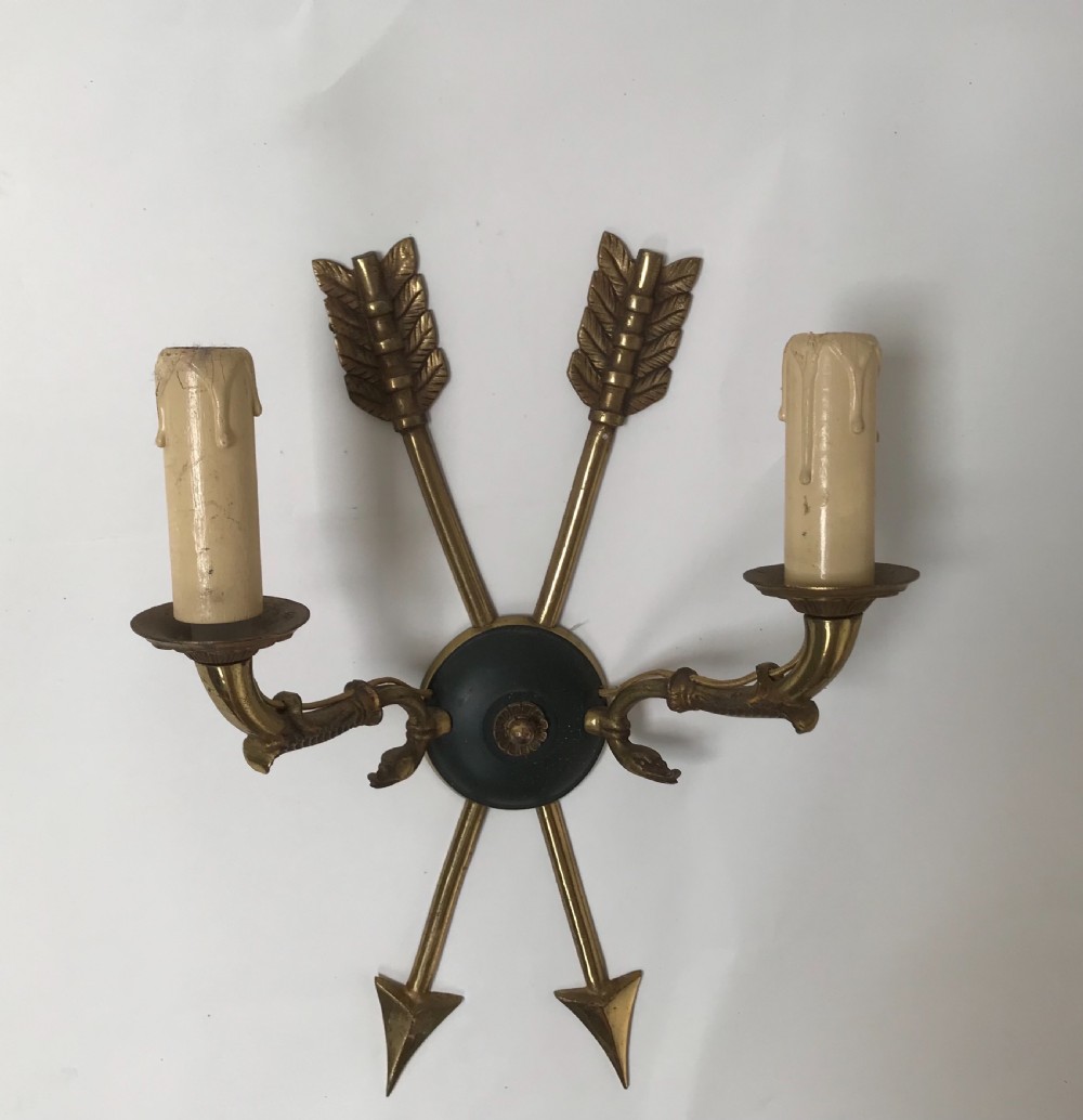 A pair of French brass twin-arm wall lights with a crossed arrow motif and dark circular backplates. View VII