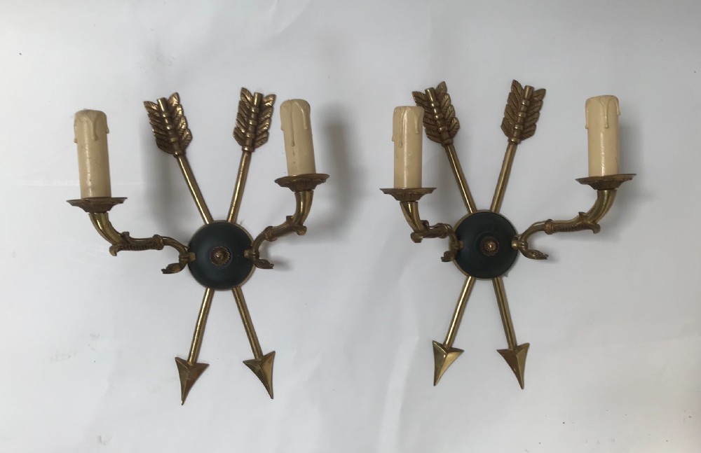 A pair of French brass twin-arm wall lights with a crossed arrow motif and dark circular backplates. View VIII