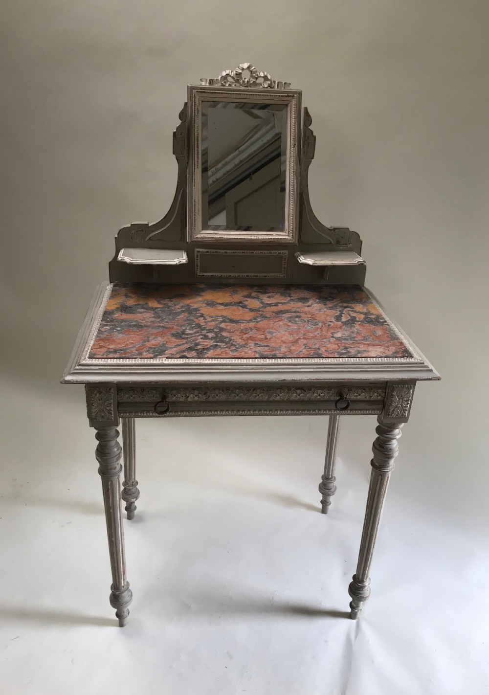 A French painted grey dressing table featuring a variegated reddish-brown marble top, an adjustable central mirror with a carved crest, two small side shelves, and tapered fluted legs. View II