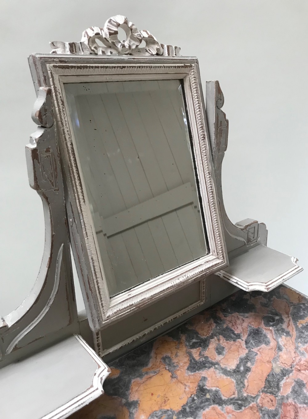 A French painted grey dressing table featuring a variegated reddish-brown marble top, an adjustable central mirror with a carved crest, two small side shelves, and tapered fluted legs. View VII