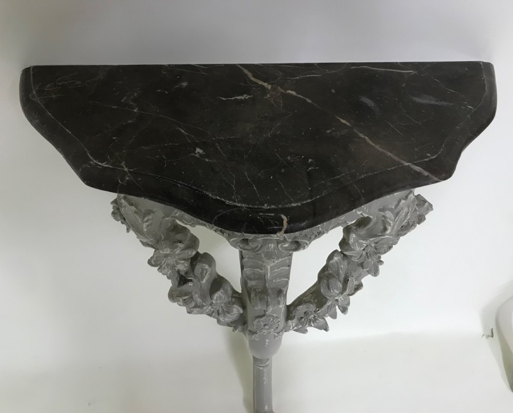 A pair of grey painted carved wood wall consoles featuring floral scroll legs and fitted black veined marble tops. View II