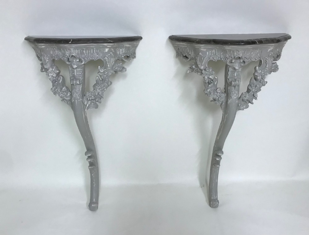 A pair of grey painted carved wood wall consoles featuring floral scroll legs and fitted black veined marble tops. View V