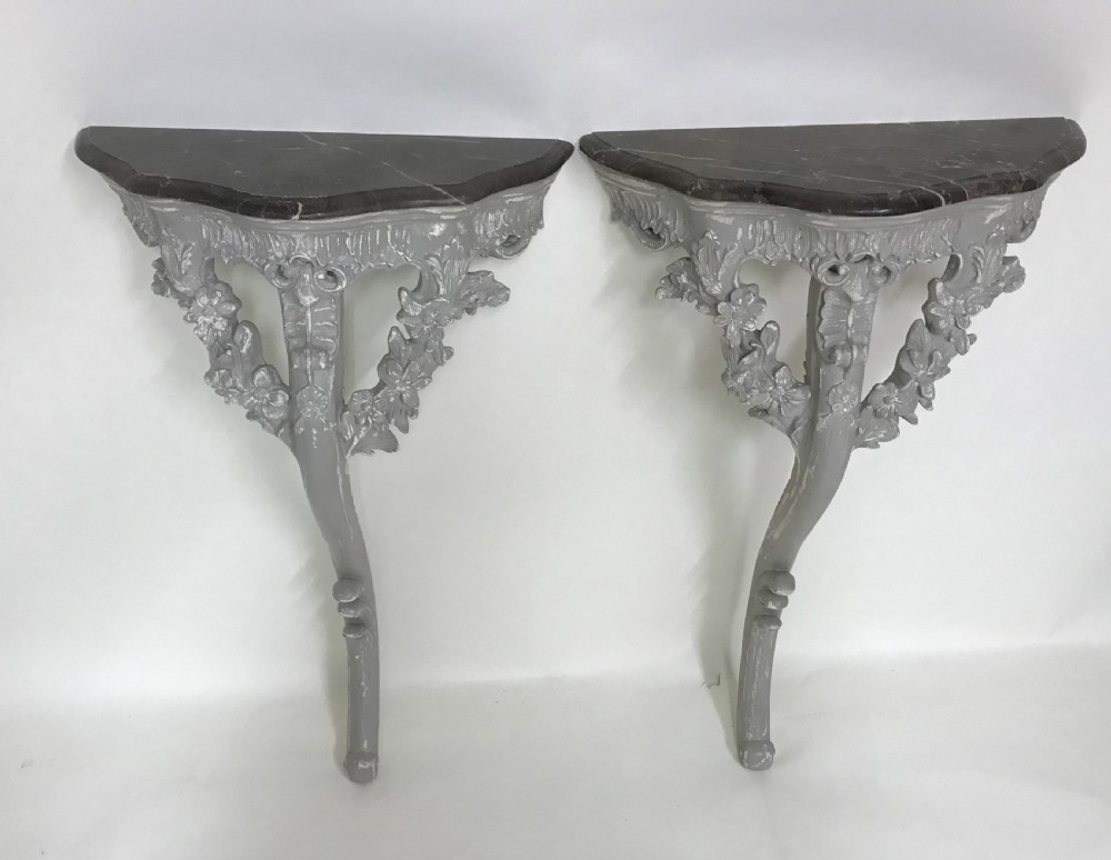 A pair of grey painted carved wood wall consoles featuring floral scroll legs and fitted black veined marble tops. View VI