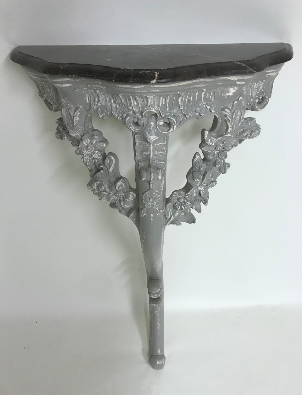 A pair of grey painted carved wood wall consoles featuring floral scroll legs and fitted black veined marble tops. View VII