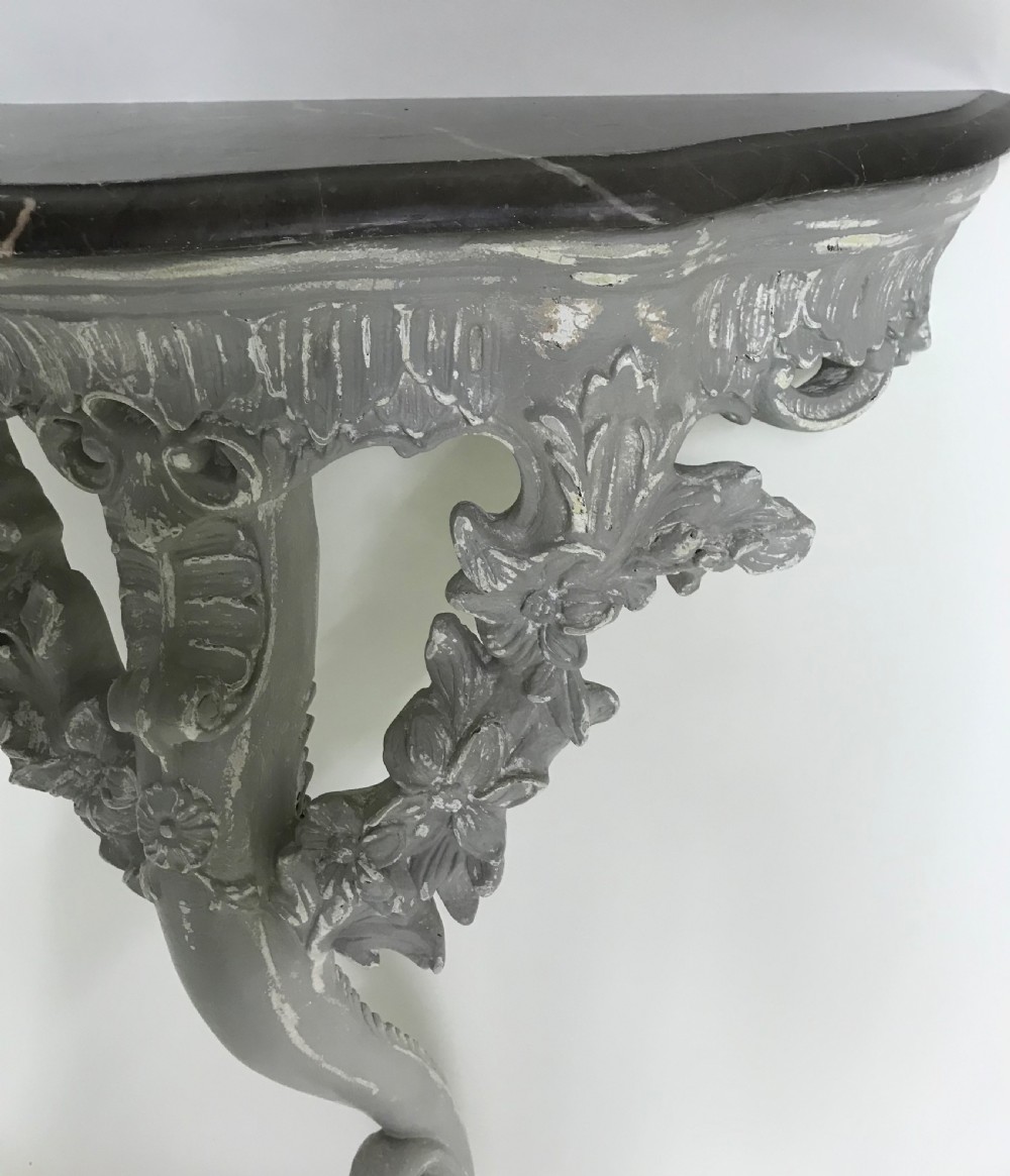 A pair of grey painted carved wood wall consoles featuring floral scroll legs and fitted black veined marble tops. View VIII