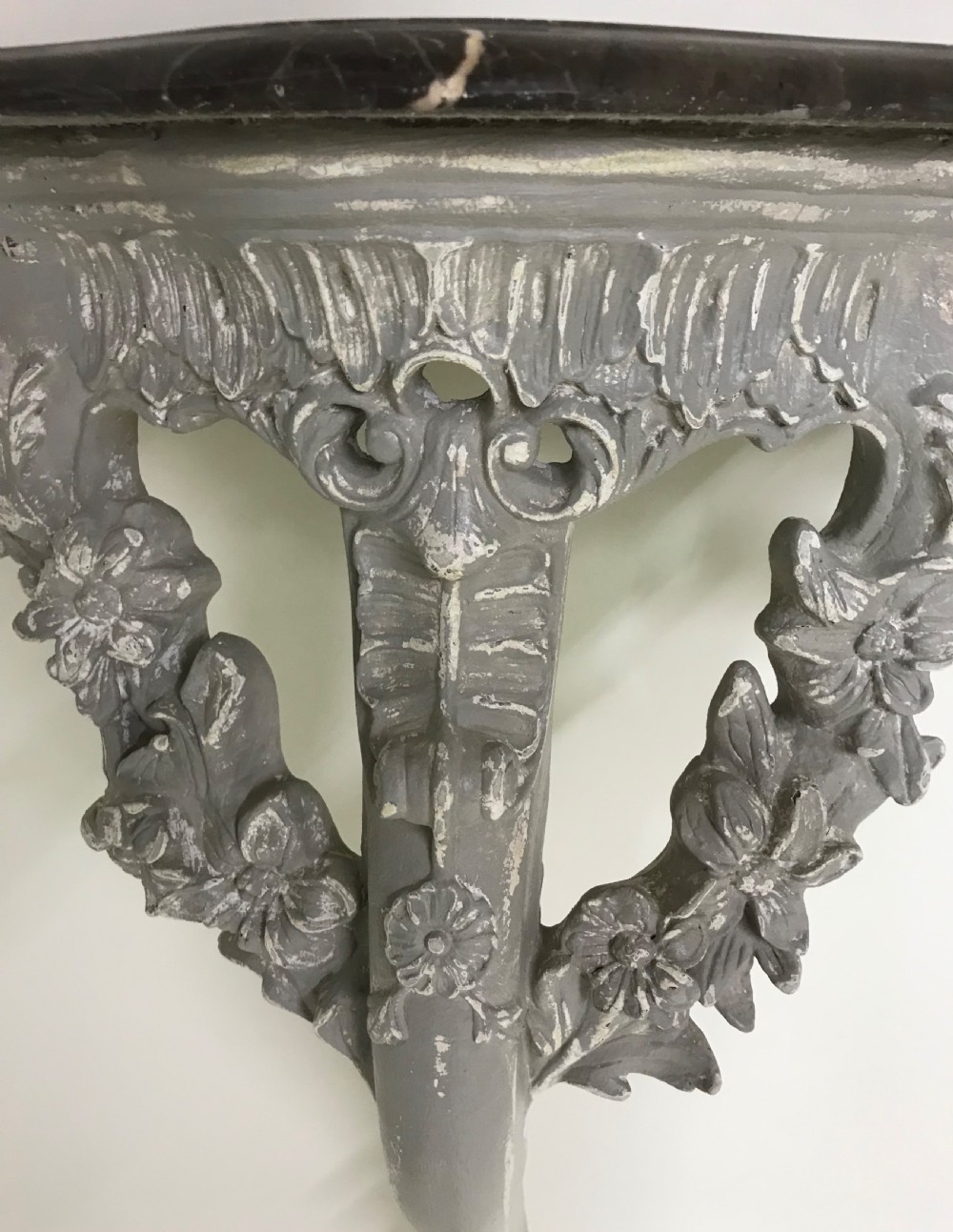 A pair of grey painted carved wood wall consoles featuring floral scroll legs and fitted black veined marble tops. View XII