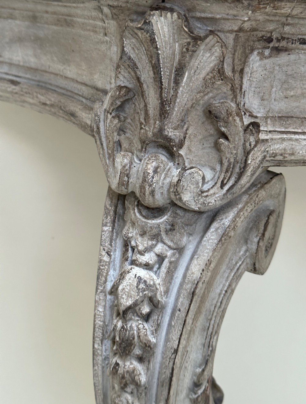A carved French style console table featuring a distressed grey painted frame, curved cabriole legs, central shell motif, and a dark marble top. View V